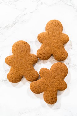 Küçük bir demet Baharatlı Zencefilli Kurabiye mermer yüzeyde düzgünce dizilmiş, tek tip şekilleri ve bayram tasarımlarını gösteren.