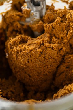 Karıştırma kabındaki koyu, koyu renkli zencefilli kurabiye hamurunun yakın çekimi, yoğun ve iyi harmanlanmış dokusunu gösteriyor. Hamur, bir sonraki yuvarlanma ve kesme adımları için hazır.