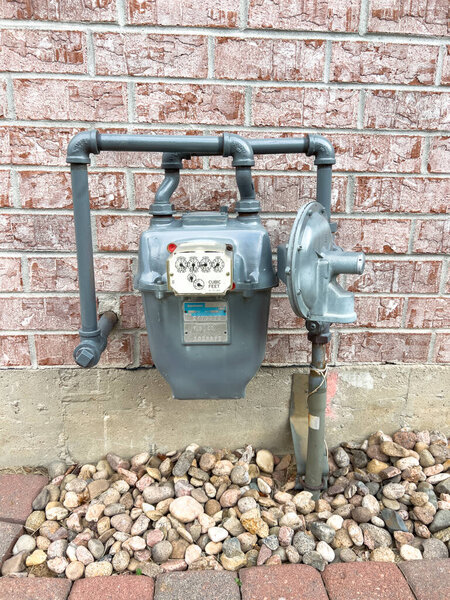 Паркер, Колорадо, США - 11 июля 2025 года - Закрытие наружного газового счетчика, прикрепленного к стене жилого дома. Четко видны трубопроводные соединения и защитный корпус. Нейтральный дневной свет