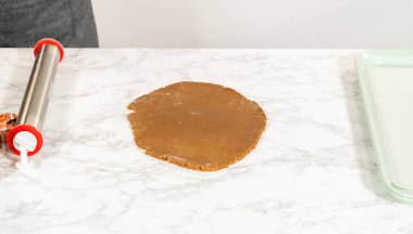 Üzerinde zencefilli ekmek hamuru bulunan mermer tezgah perspektifi incelenmiş ve kurabiye şekillendirmek için yakınlarda duran kurabiye kesiciler var..