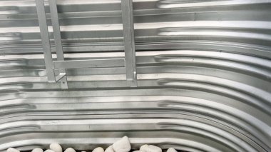 Metal bir pencerenin tabanındaki temiz, beyaz, dekoratif çakıl taşlarının yakın çekimi. Metalik duvarlar, etrafındaki yumuşak ışığı yansıtıyor..