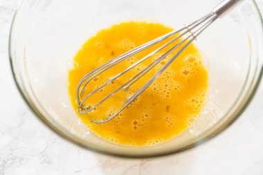 Klasik Şekerli Kurabiye Hamuru için hazırlanmış çırpılmış yumurtaların içinde dinlenen çırpılmış çırpı çırpıcının yakından görüntüsü. Yumurtalar iyi karıştırılmış ve hafif köpüklü. Hamur karışımına eklenmeye hazır.