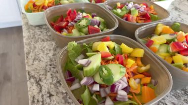 Kamera, dilimlenmiş salatalık, dolma biber, soğan ve yeşilliklerle dolu birkaç salata kabının tepe açısını gösteriyor. Her salata taze ve dikkatlice hazırlanmış görünüyor..