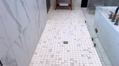 İçinde siyah metal saplar ve armatürlerin olduğu geniş ölçekli bir mermer duş. Arka planda küçük bir ahşap bank ve katlanmış havlular görülebilir..