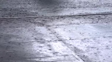 Macro tarzı yağmur damlaları ıslak beton kaldırım yüzeyine çarpıyor. Yakından bakıldığında zemin dokusu ve doğal ışık altında saçılmış damlacıklar vurgulanıyor..