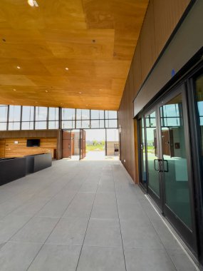 Açık havada oturma odası ve kulüp binasının içinde uzun pencereler olan parlak bir salon. Odada ahşap panelli tavan ve minimalist mobilyalar bulunuyor..