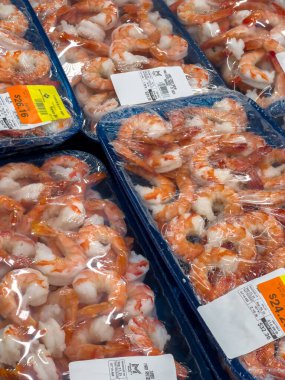 Castle Rock, CO, ABD-27 Eylül 2025 - Dondurulmuş süpermarket bölümündeki mavi plastik tepsilerde paketlenmiş çiğ karides sergileniyor. Karidesler düzgünce düzenlenmiş, etiketler görünür, altında