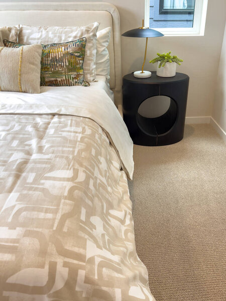 Уютная спальня с кроватью с узорчатыми постельными принадлежностями и черной тумбочкой с декором. Современный дизайн стильный и удобный.