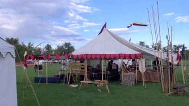 Sedalia, CO, Usa-Eylül 20, 2025 - Yavaş Hareket - Çimlerin üzerinde kırmızı süslemeli çadır, ahşap yapılar ve içinde eşyalar var. Sahne parlak ve açık, bayraklar ve direklerle