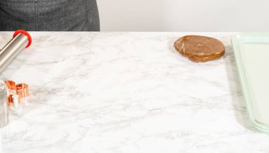 Fırın aletleri ve yuvarlak bir top zencefilli ekmek hamuru yuvarlanmaya hazır. Aletler arasında mermer bir yüzeye yerleştirilmiş merdane iğnesi, kurabiye keskisi ve un kabı yer alıyor..