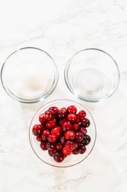 Cam bir kasede taze kızılcık resmi, şeker ve diğer malzemelerle eşleştirilmiş, yaban mersini yemekleri veya tatil tarifleri için ideal..