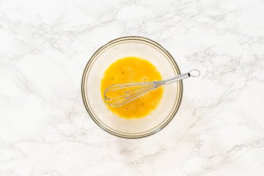 İçinde çırpılmış yumurta ve klasik şekerli kurabiye hamuru karışımında çırpılmış çırpılmış çırpılmış çırpı kabıyla mermer bir yüzey üzerinde duran vanilya özlü cam kase. Bu basamakta ıslak malzeme hazırlığı çok önemli.