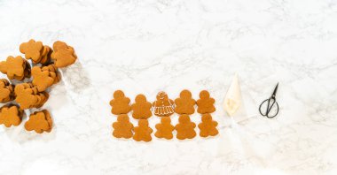Gingerbread girl cookies are evenly spread out in rows, surrounded by tools and supplies for decorating.
