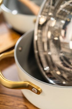 Beyaz seramik bir tencerede altın saplı paslanmaz çelik bir buharlı makro çekim. Ayrıntılı dokular ve ışık yansımaları mutfak sahnesine derinlik ekler.