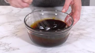 Elleri, içinde ıslak malzemeler olan cam bir kaseye koyu koyu şerbet döker. Kase beyaz bir mermer tezgahın üzerinde duruyor..