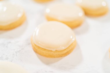 Bir yığın taze pişmiş şeker kurabiyesi pürüzsüz, parlak bir katman kraliyet kreması ile parşömen kağıdında kurutuluyor. Kurabiyeler şekil ve boyut olarak aynı, görsel olarak çekici bir sunum oluşturuyorlar.