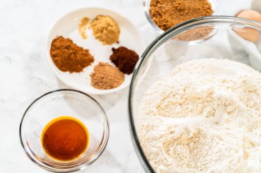 Çukulatalı Zencefilli Kurabiye Kurabiyesi Hamuru için baharat, tereyağı ve pekmez gibi diğer malzemelerle birlikte mermer bir yüzeye yerleştirilmiş elek ile dolu büyük bir cam karıştırma kabı..