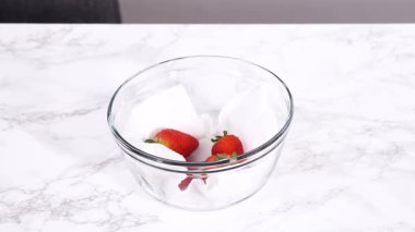 İki el, beyaz mermer bir yüzey üzerinde bir kase çileğin üzerine şeffaf plastik ambalaj gerer. Sahne, yumuşak ve tarafsız bir ses tonuyla bir ev mutfağında geçiyor..