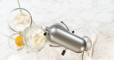 Tereyağı ve şekerin gümüş bir büfede çırpılmış vaziyette, un kaseleri ve çırpılmış yumurtalarla birlikte görünümü. Arka planda temiz bir mermer tezgah var..