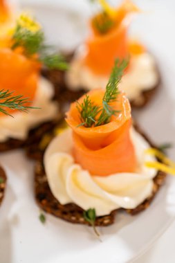 Çıtır bir krakerin üzerine zarif bir şekilde yerleştirilmiş füme somon kanalı. Üstünde krem peyniri, taze kekik ve zeytinyağı var. Canlı portakal somonu kontrastları