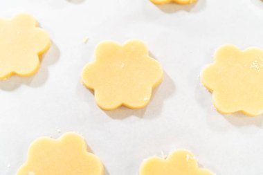 Çukur merkezli, çiçek şeklinde bir kurabiyenin keskin yakın çekimi temiz kenarları ve pürüzsüz hamuru gösteriyor. Paskalya Kurabiyesi Sandviçi için mükemmel ahududu kremalı.