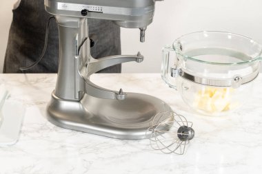 İçinde tereyağı bulunan cam bir karıştırma kabıyla limonlu kurabiye yapmaya hazır bir tezgah hazırlandı. Kablo çırpma eklentisi karıştırma işlemi için hazırlandı.