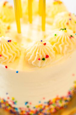 Doğum günü pastalarının yakın plan fotoğrafı. Üzerinde uzun sarı mumlar olan kremalı şekerlemeler. Boru şeklindeki krema gökkuşağı parçacıklarıyla süslenir ve yumuşak ışık hafif bir parıltı verir..