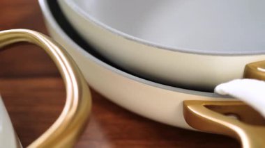 Kırmızı çizgili beyaz bir mutfak havlusuna yakın bir yerde altın bir tava sapı gösterilir. Kompozisyonda temiz malzemeler ve modern tasarım vurgulanıyor.