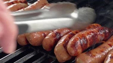 Yavaş hareket et. Sıcak ızgarada pişen sulu sosisler altında ızgara izleri ve alevler var. Sahne, açık havada gün ışığıyla birlikte cızırdayan etleri yakalıyor..