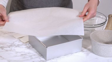 Bir insan gümüş kare bir tavanın içine parşömen kağıdı koyar. Arka planda karıştırma kapları görünür.