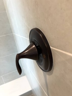 Koyu bronz bir duş kabzası aydınlık bir duvara monte edilir. Temiz çizgiler ve zıt bitiş modern bir banyo estetiği sağlıyor..