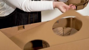 Parker, Colorado, ABD-6 Mayıs 2025 - Bir kadın yemek takımını çıkardıktan sonra büyük bir paket kutusundan iç karton parçaları çıkarıyor. Video, paketleri açma sürecinde temiz bir adım yakalar