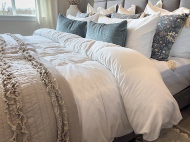 Karanlık, modern bir komodinin yanında püsküllü atımlı ve dekoratif yastıklı iyi giyimli bir yatağın yan perspektifi. Ürün modelleri ya da iç tasarım fikirleri için harika..