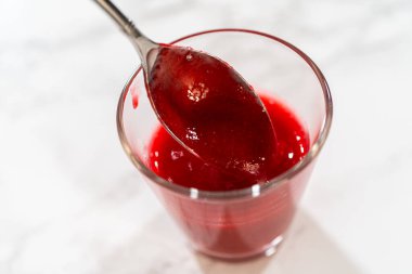 Canlı kırmızı renk ve dokuya odaklanmış taze ahududu püresiyle dolu bir kavanozun üzerinde bir kaşık kaldırıldı. Paskalya Kurabiyesi Sandviçi için kullanışlı, ahududu kremalı ve fırın sahneli..