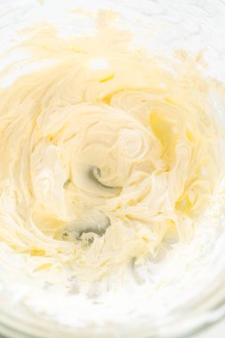 Kusursuzca çırpılmış pürüzsüz ve havadar krem peynirin yakın çekim görüntüsü. Yumuşak doku ve zengin renk cam karıştırma kabında vurgulanır, yayılmak için ideal tutarlılığı gösterir