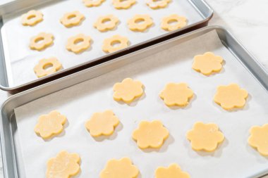 Two metal baking trays filled with flower-shaped cookies, both with and without centers, prepped for baking. Ideal setup for Easter Cookie Sandwich with Raspberry Buttercream.