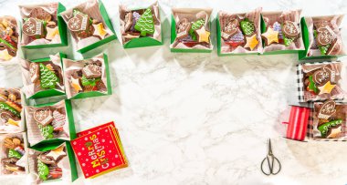 Noel kurabiyesinin hediye kutusunu saran, güzelce hazırlanmış Noel kutuları ile çevrili, tepeden tırnağa bir el resmi. Sahnede zencefilli kurabiye, şenlikli ambalajlar ve