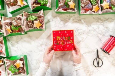 Noel kurabiyesinin hediye kutusunu saran, güzelce hazırlanmış Noel kutuları ile çevrili, tepeden tırnağa bir el resmi. Sahnede zencefilli kurabiye, şenlikli ambalajlar ve