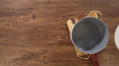 Altın saplı beyaz bir seramik kap, ahşap bir masanın ortasında duruyor. Görüntü, yumuşak doğal ışıklandırmayla yukarıdan aşağıya doğru bir kompozisyona sahip..