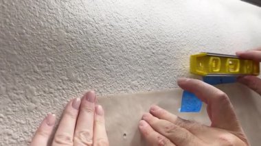 Süpürge, CO, USA-152 - 25 Ocak 2025 - Bir tuvalet duvarında kağıt şablon tutmak için mavi boya bandı uygulayan bir grup el. Hizalama için bir seviye aracı yakınlarda.
