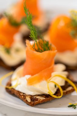 Çıtır bir krakerin üzerine zarif bir şekilde yerleştirilmiş füme somon kanalı. Üstünde krem peyniri, taze kekik ve zeytinyağı var. Canlı portakal somonu kontrastları