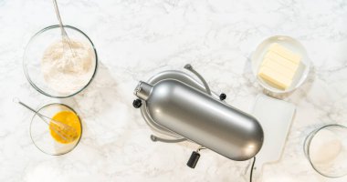 Bir kalıp tereyağı, çırpı ve kesim tahtasının yanında un ve yumurta karışımıyla dolu bir kâse. Fırın, parlak mermer bir yüzeye kurulmuş..