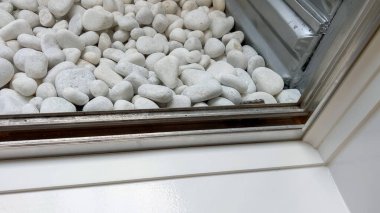 Bodrum penceresinden bakıldığında düzgün yerleştirilmiş beyaz dekoratif taşların kavisli alüminyum bir pencereye yerleştirildiğini görüyoruz. Sahne parlak ve düzenli..