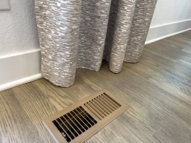 Gri desenli perdelerin bir kısmı ahşap kaplama döşemeye asılı. Alan parlak ve asgari düzeyde..