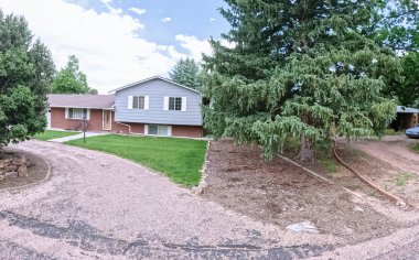 Kıvrımlı çakıl yolu ve yamalı yeşil çimenliği olan iki katlı bir banliyö evi. Olgun peyzaj ve parlak gün ışığında büyük ağaçlarla çevrili..