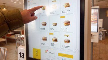 Parker, Colorado, ABD-25 Ocak 2025 - Yeşil ceketli bir adam fast food restoranındaki dijital bir büfede kahvaltı sandviçi sipariş ettiğini söylüyor. Dokunmatik ekranda fiyatlar ve resimler