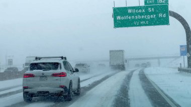 Parker, Colorado, ABD-9 Ocak 2025 Broomfield, Colorado 'da sınırlı görüş mesafesi olan karla kaplı bir yolda bir SUV sürüyor. Kar yağışı devam ederken tekerlek izleri buzun içinden görülebiliyor..