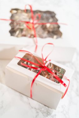 Bir el, canlı kırmızı bir kurdeleyle bağlanmış güzel paketlenmiş tatil kurabiyesi kutusunu tutar. İçerde, çeşitli dekore edilmiş zencefilli kurabiyeler temiz pencereden içeri bakıyor ve bunu yenilebilir mükemmel bir hediye yapıyor.