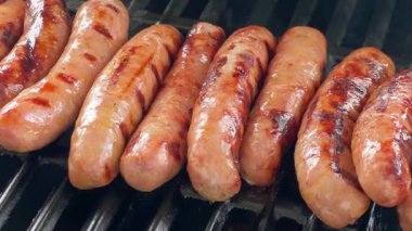 Yavaş hareket et. Izgara sosisleri yakın çekim ve belirgin ızgara izleri. Sosisler sıcak ızgaranın üzerine sıkıca yerleştirilmiş taze dokuları ve zengin renkleri gösteriyor..