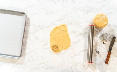 Un kaplı bir yüzeye sarılmış kurabiye hamuru. Çiçek şekilleri kesilmiş. Ahududu kremalı Paskalya Kurabiyesi Sandviçi yapmaya hazır. Yemek tarifi blogları, kurabiye dersleri ve bahar temalı